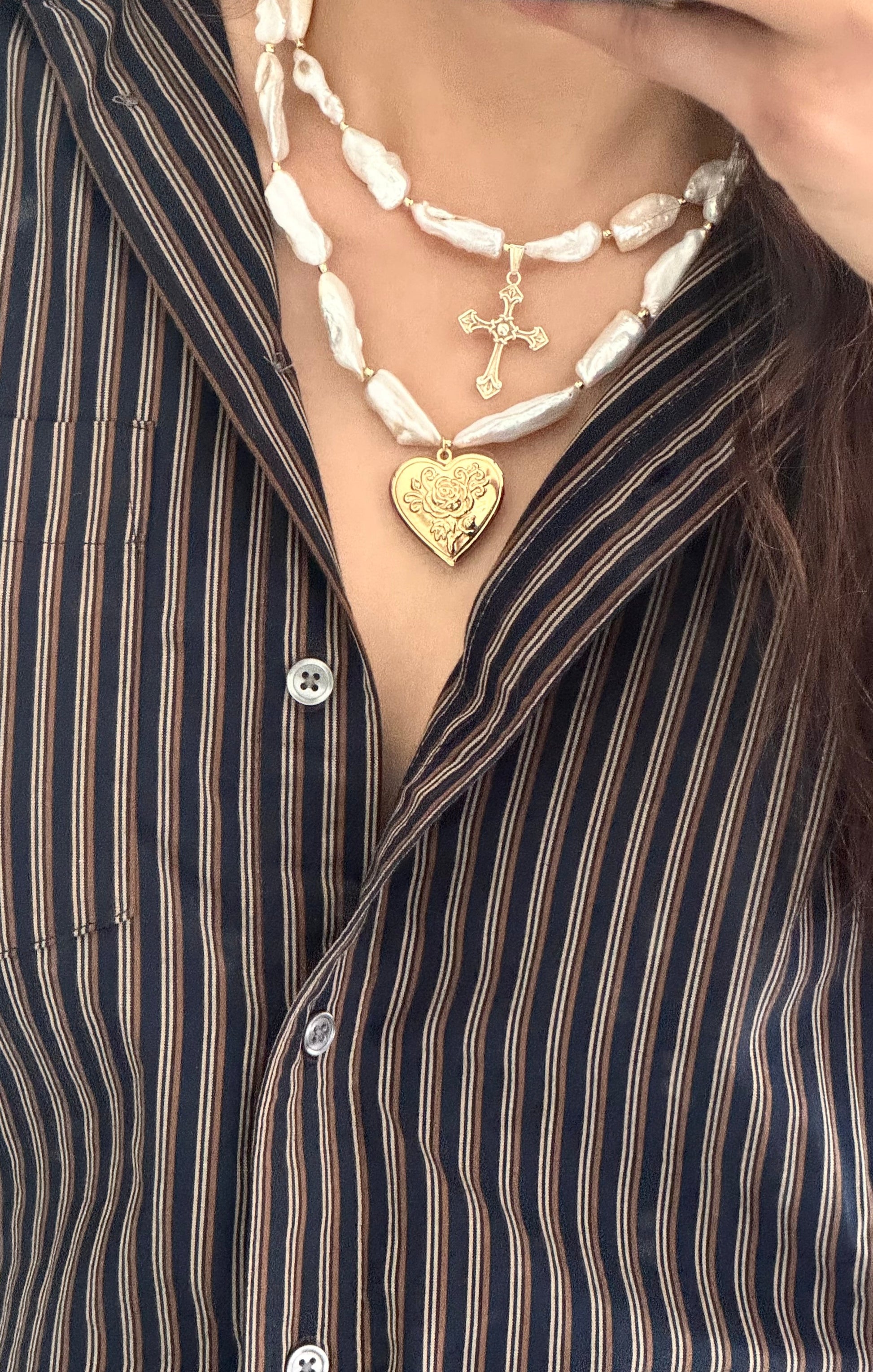 Close-up of layered necklaces with a focus on a gold heart pendant, worn over a striped shirt.